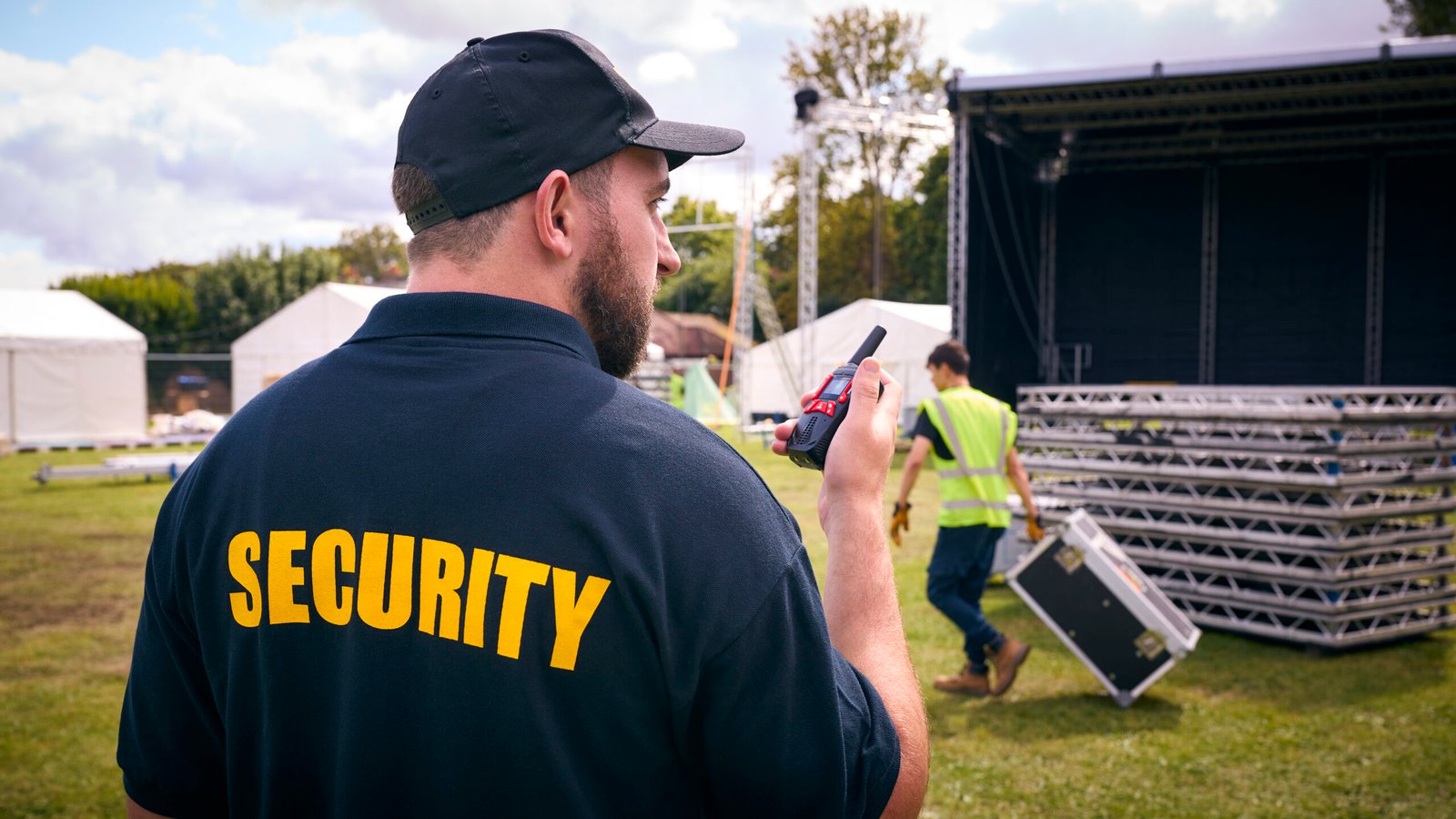 Security Team At Outdoor Stage For Music Festival Or Concert Talking Into Radio